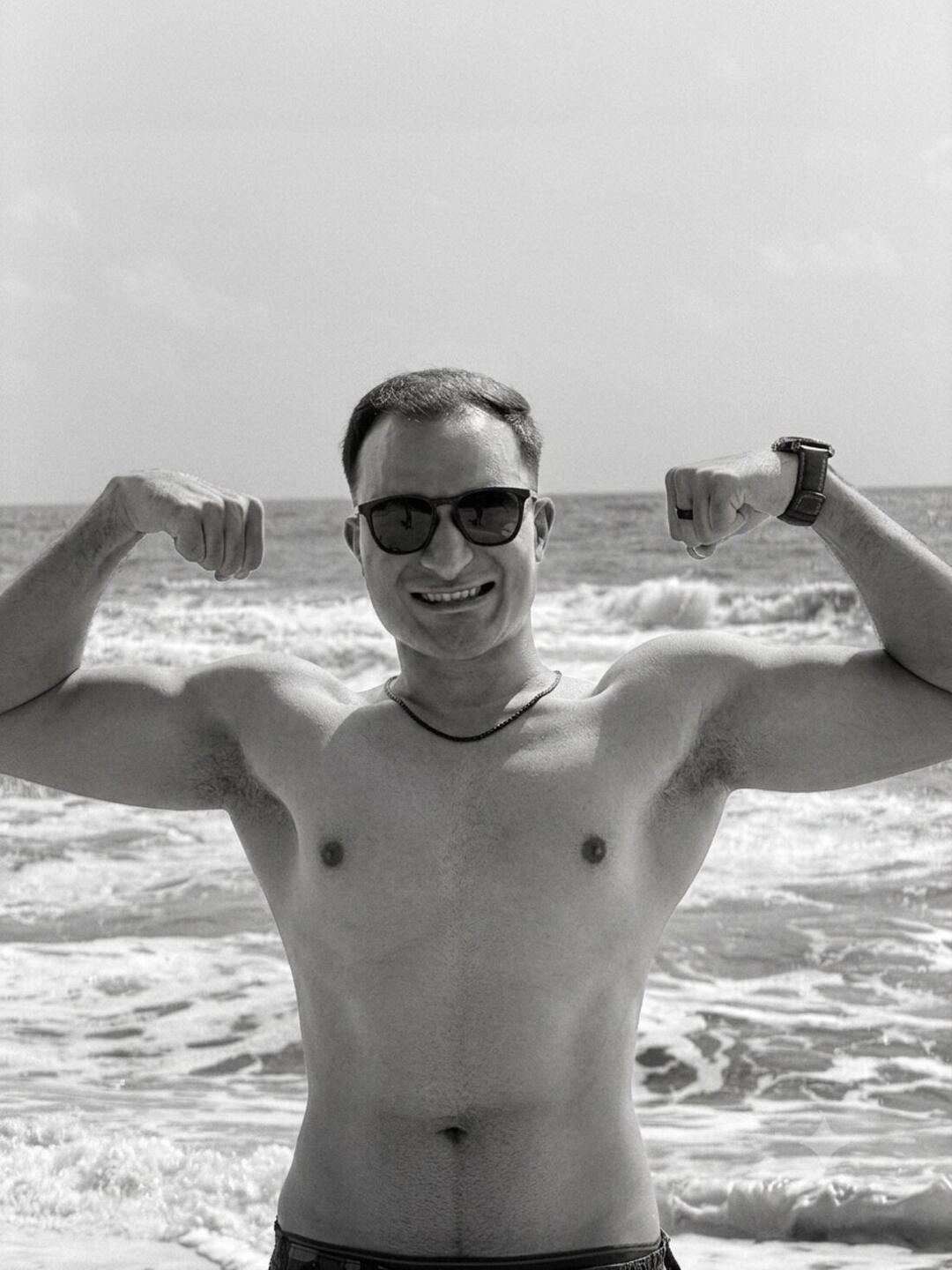 Nikhil at the beach, flexing, the ocean and waves behind him.